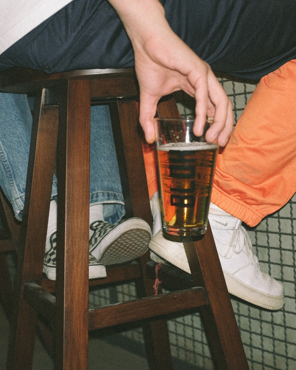 person holding clear drinking glass with brown liquid
